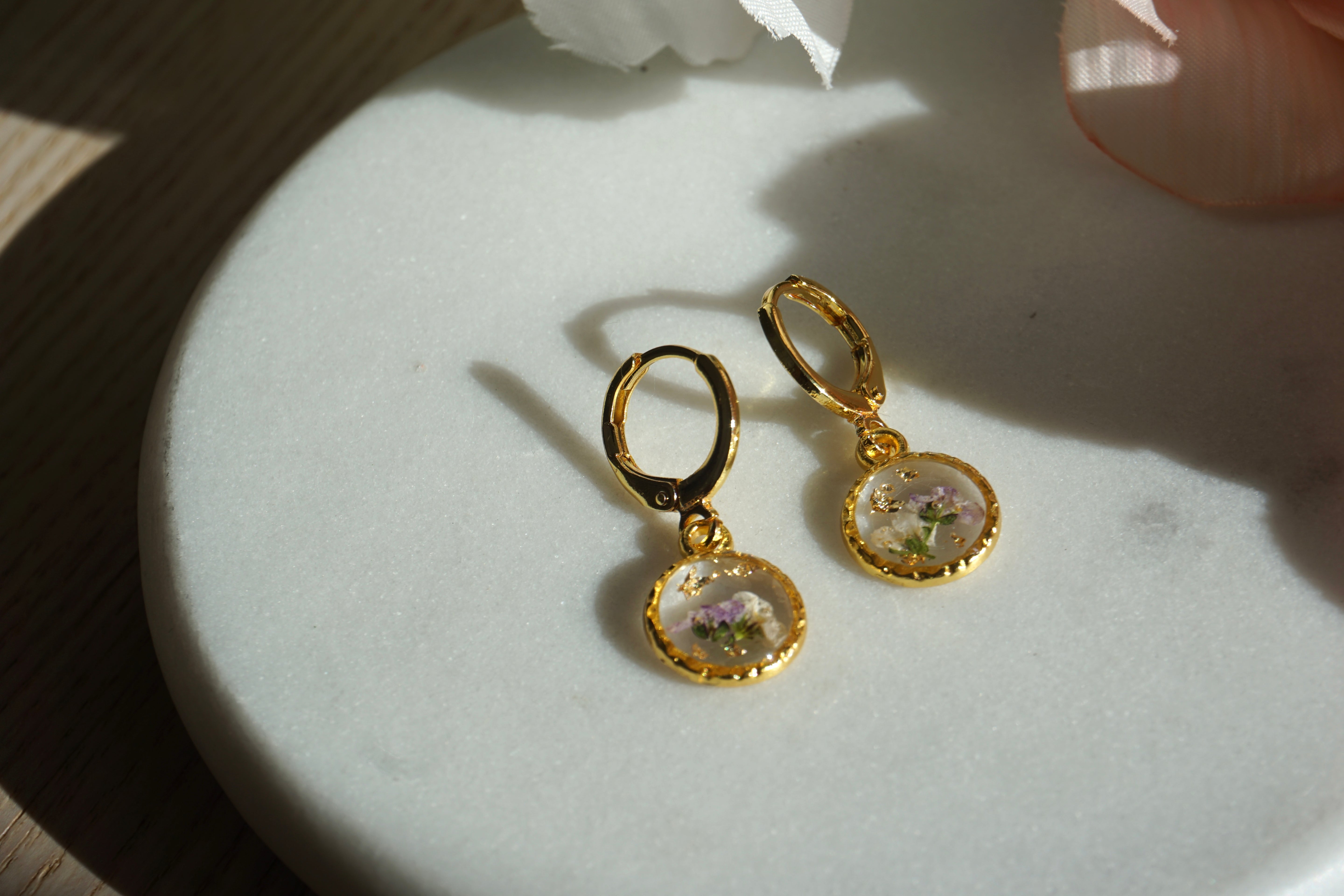Gold earrings with floral designs on a light surface