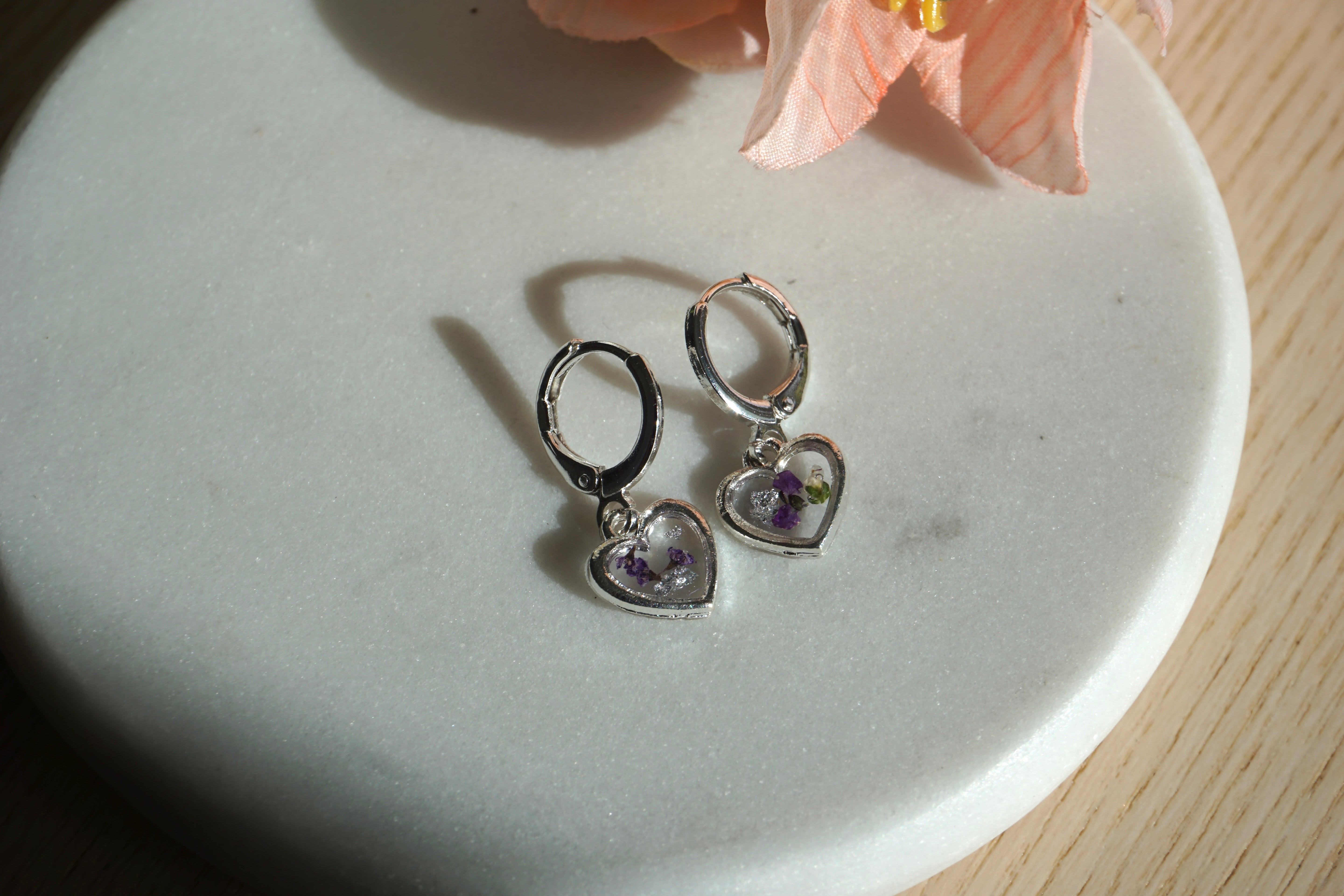 Heart-shaped silver earrings on a white plate with a pink flower in the background