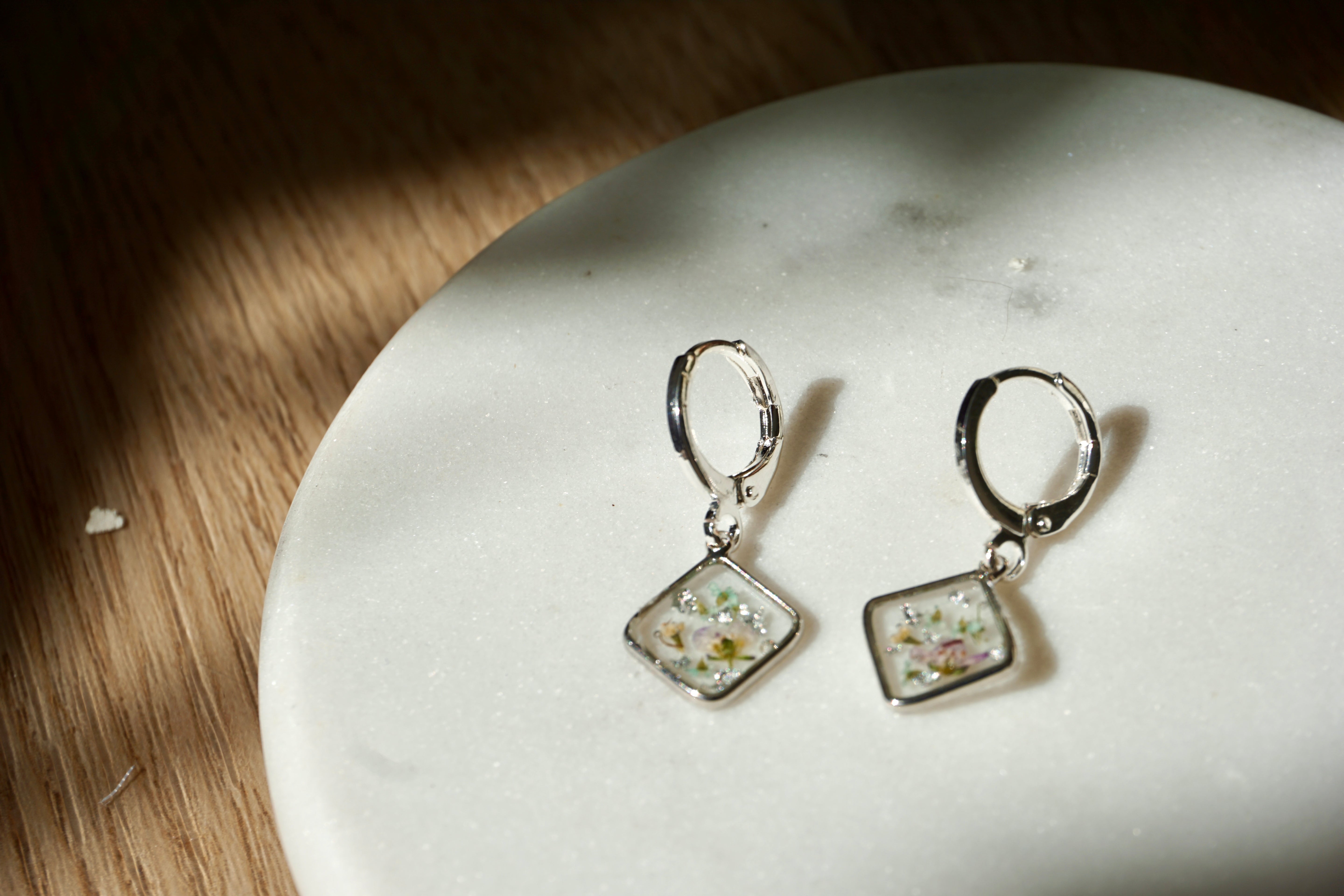 Silver earrings with floral designs on a white stone surface