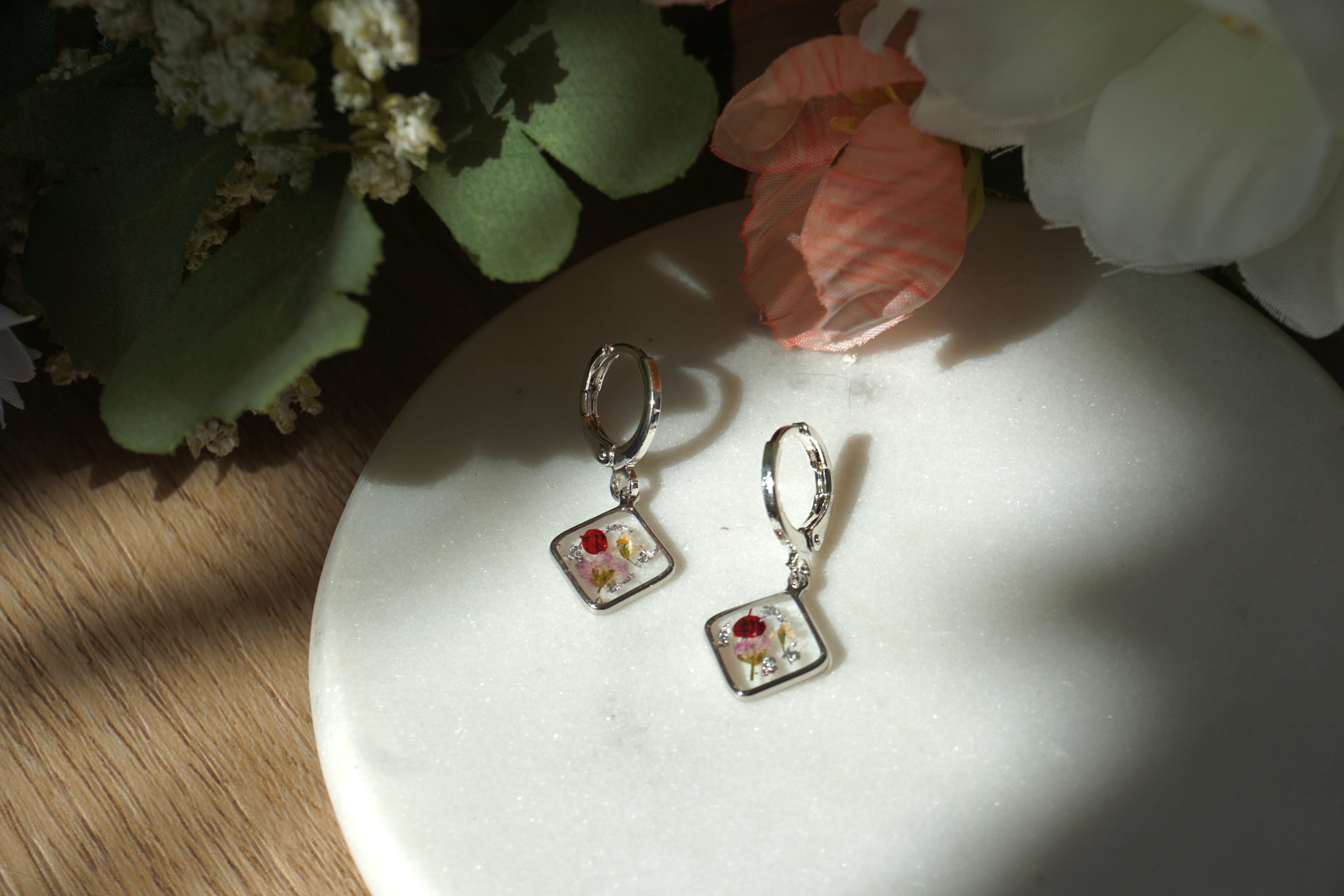 Pair of earrings on a white surface with flowers in the background