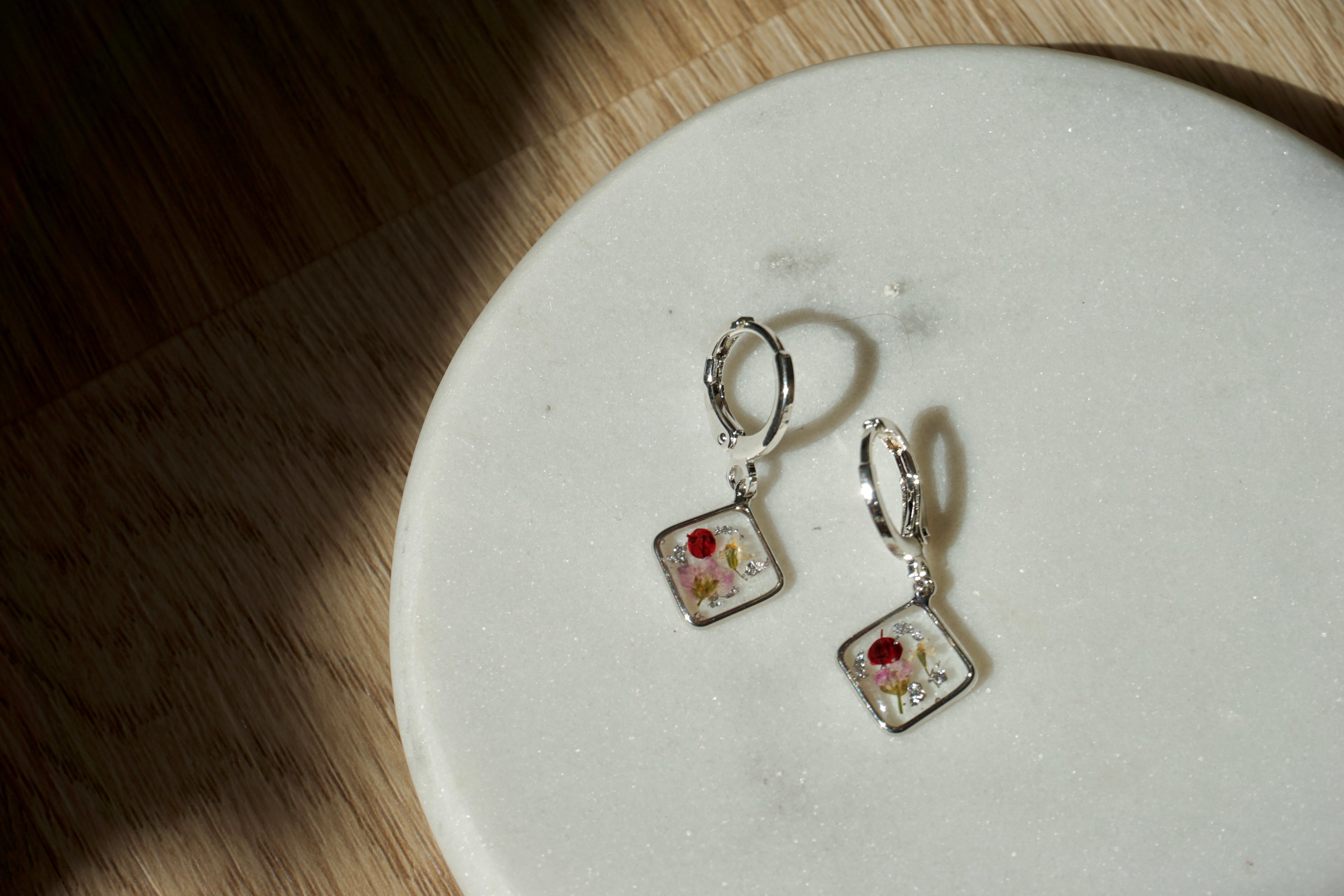 Pair of square-shaped earrings with floral design on a white plate.