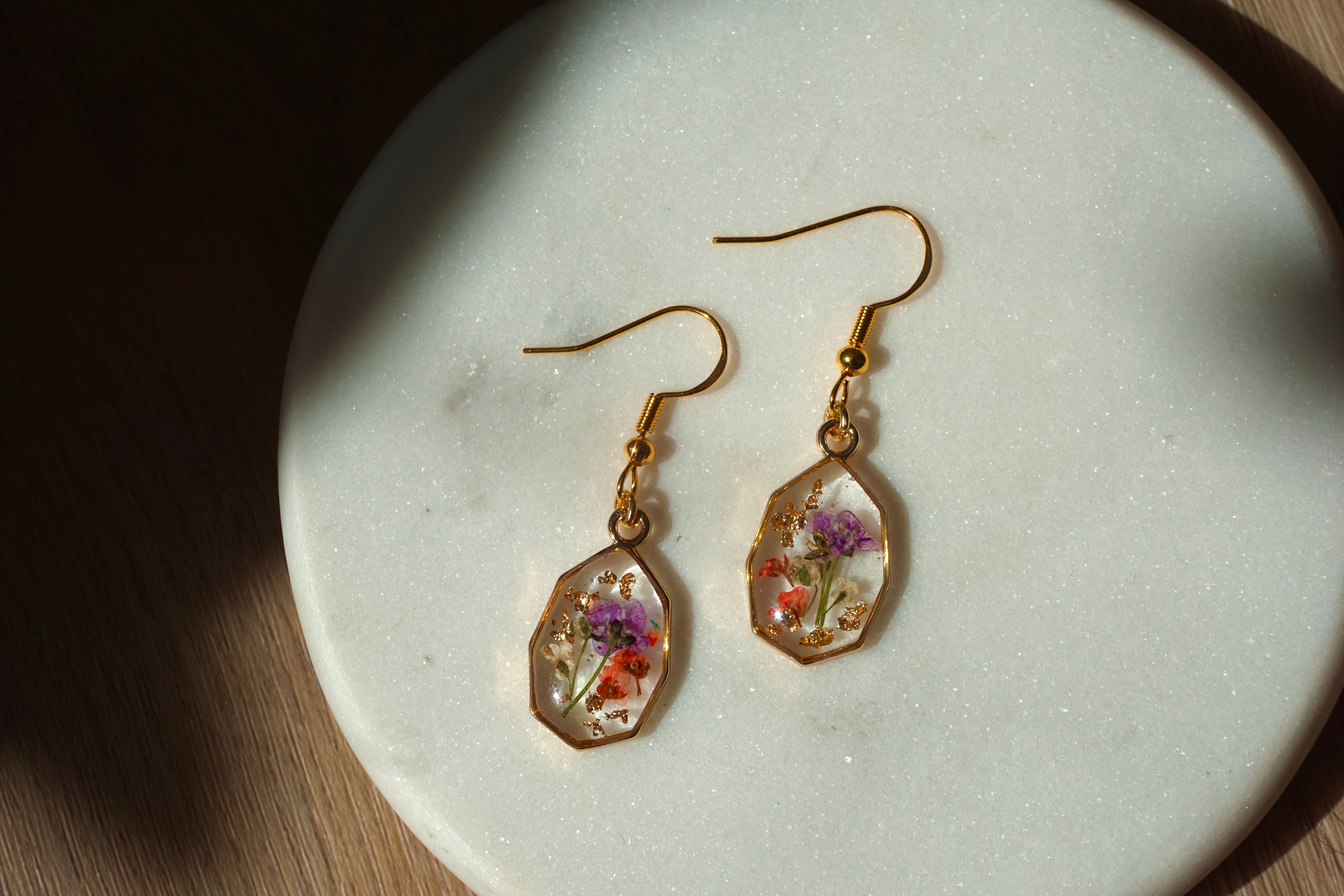 Gold earrings with embedded flowers on a light stone surface