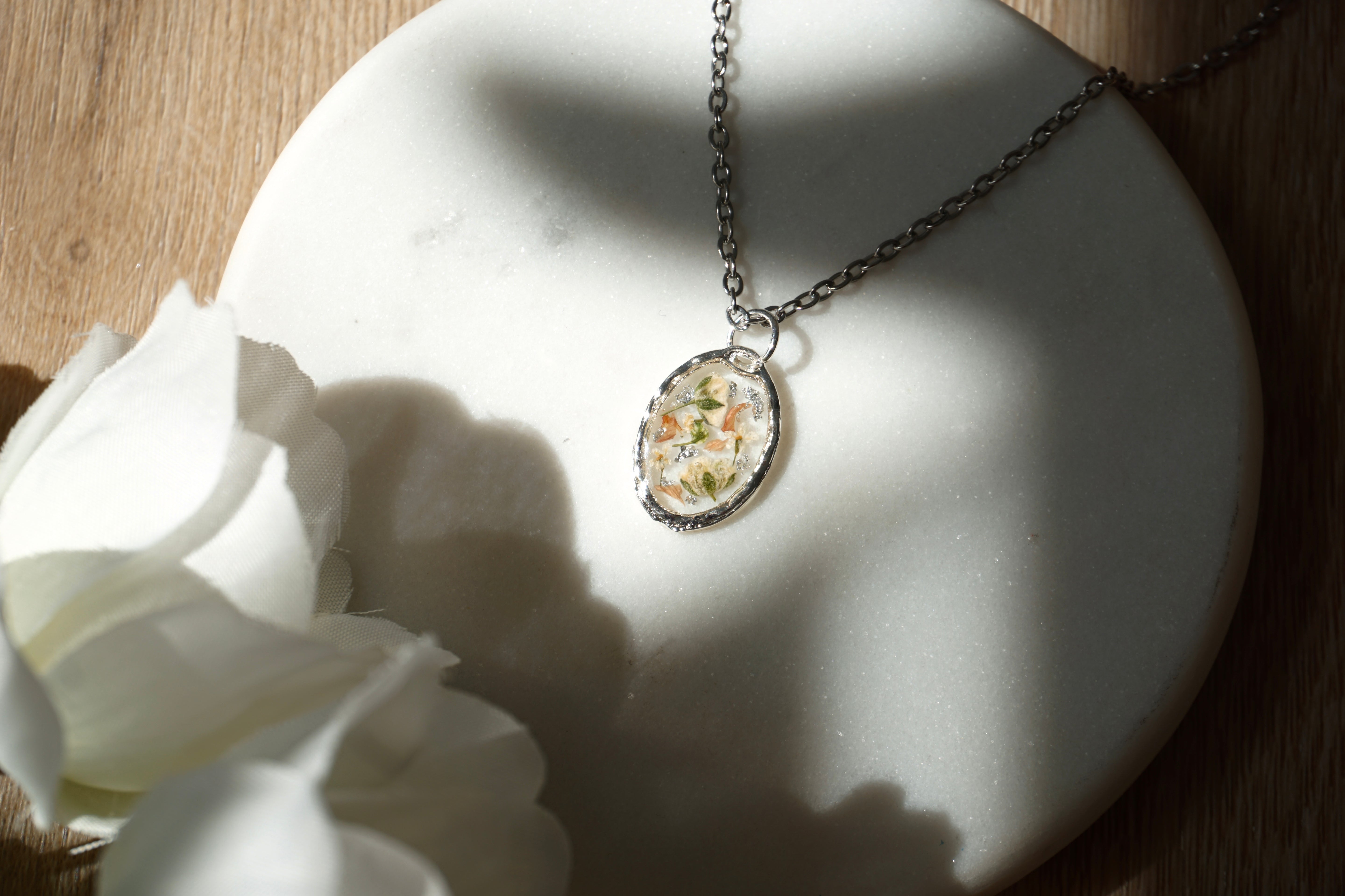 Necklace with a pendant on a white stone surface next to white flowers