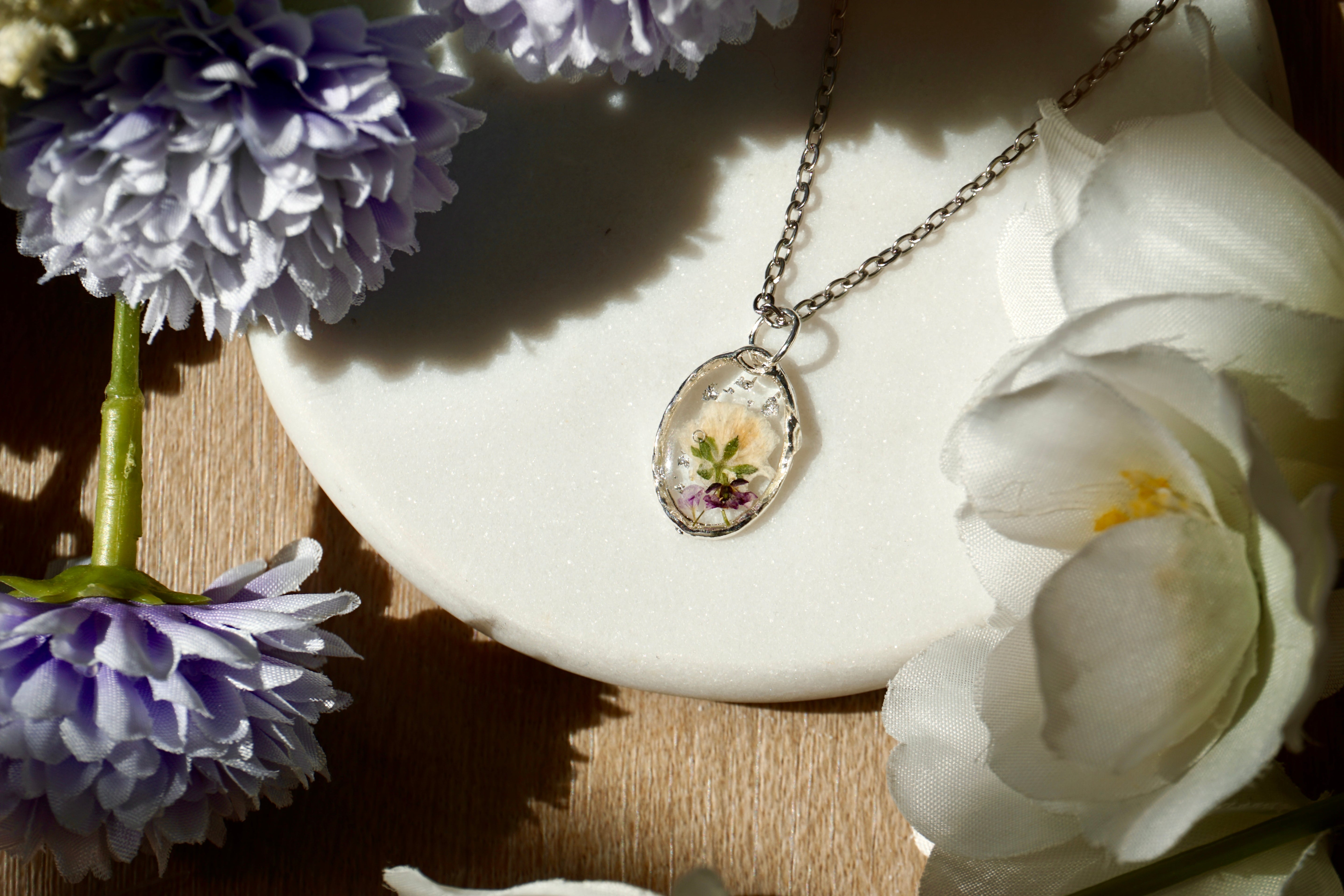 Necklace with a floral pendant on a white dish surrounded by flowers