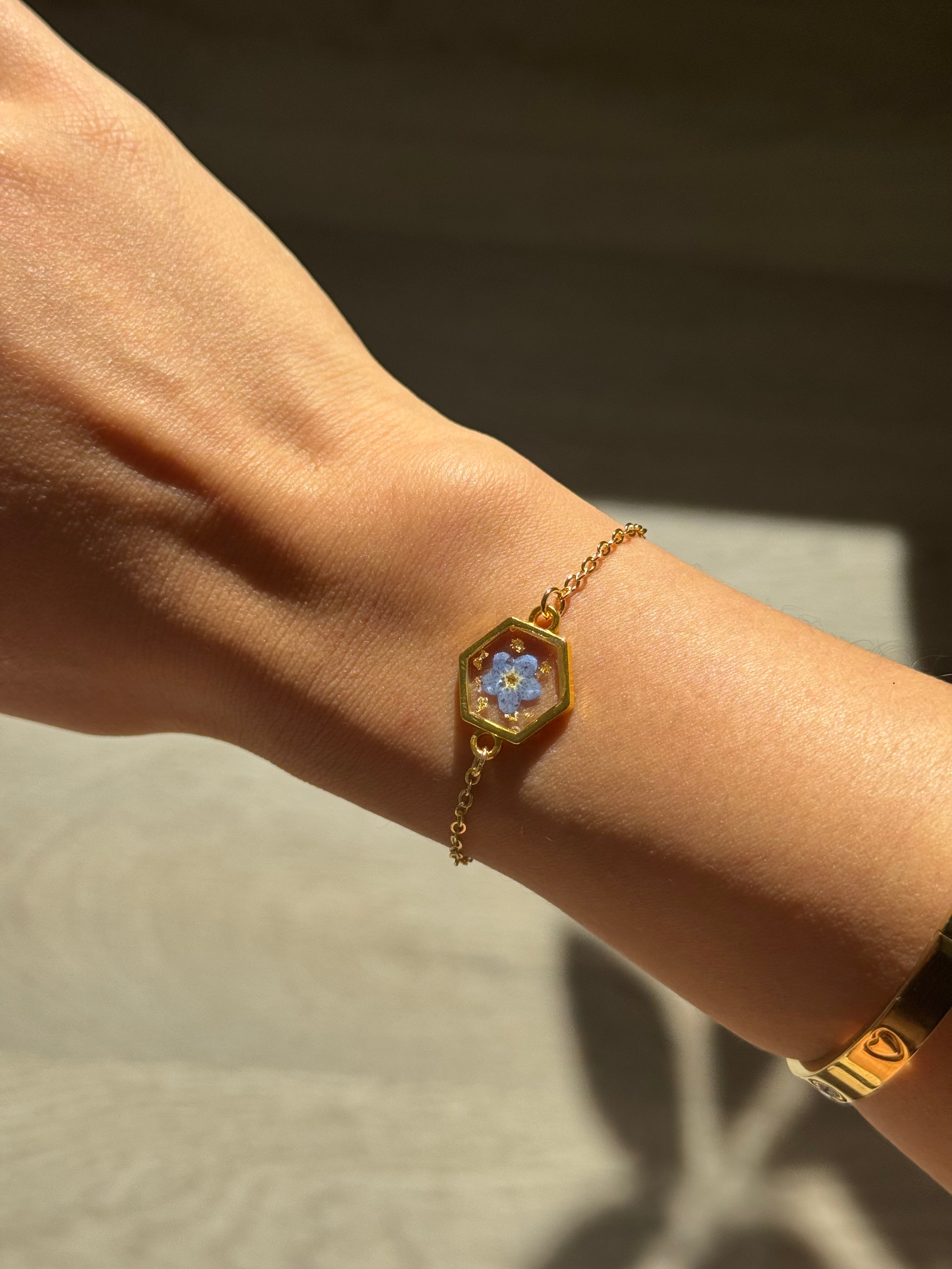 Gold bracelet with a floral design on a wrist against a neutral background