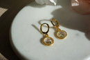 Gold earrings with floral designs on a light surface