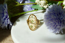 Gold ring with floral design on a white plate surrounded by flowers