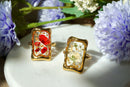 Gold-framed rings with floral designs on a white surface surrounded by flowers.
