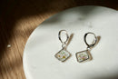Silver earrings with floral designs on a white stone surface