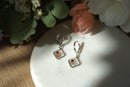 Pair of earrings on a white surface with flowers in the background