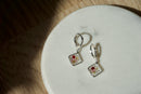 Pair of square-shaped earrings with floral design on a white plate.