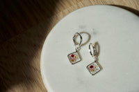 Pair of square-shaped earrings with floral design on a white plate.