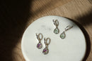 Teardrop-shaped earrings with gemstones on a white marble surface.