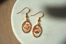 Gold earrings with floral designs on a white plate