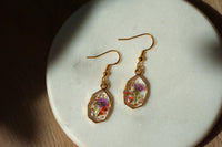 Gold earrings with embedded flowers on a light stone surface