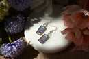 Pair of floral earrings on a white stone surface with flowers around
