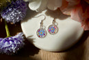 Pair of floral earrings on a white stone with flowers around
