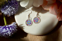 Pair of floral earrings on a white stone with flowers around