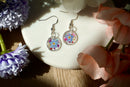 Colorful floral earrings on a white dish with flowers around
