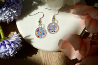 Colorful floral earrings on a white dish with flowers around