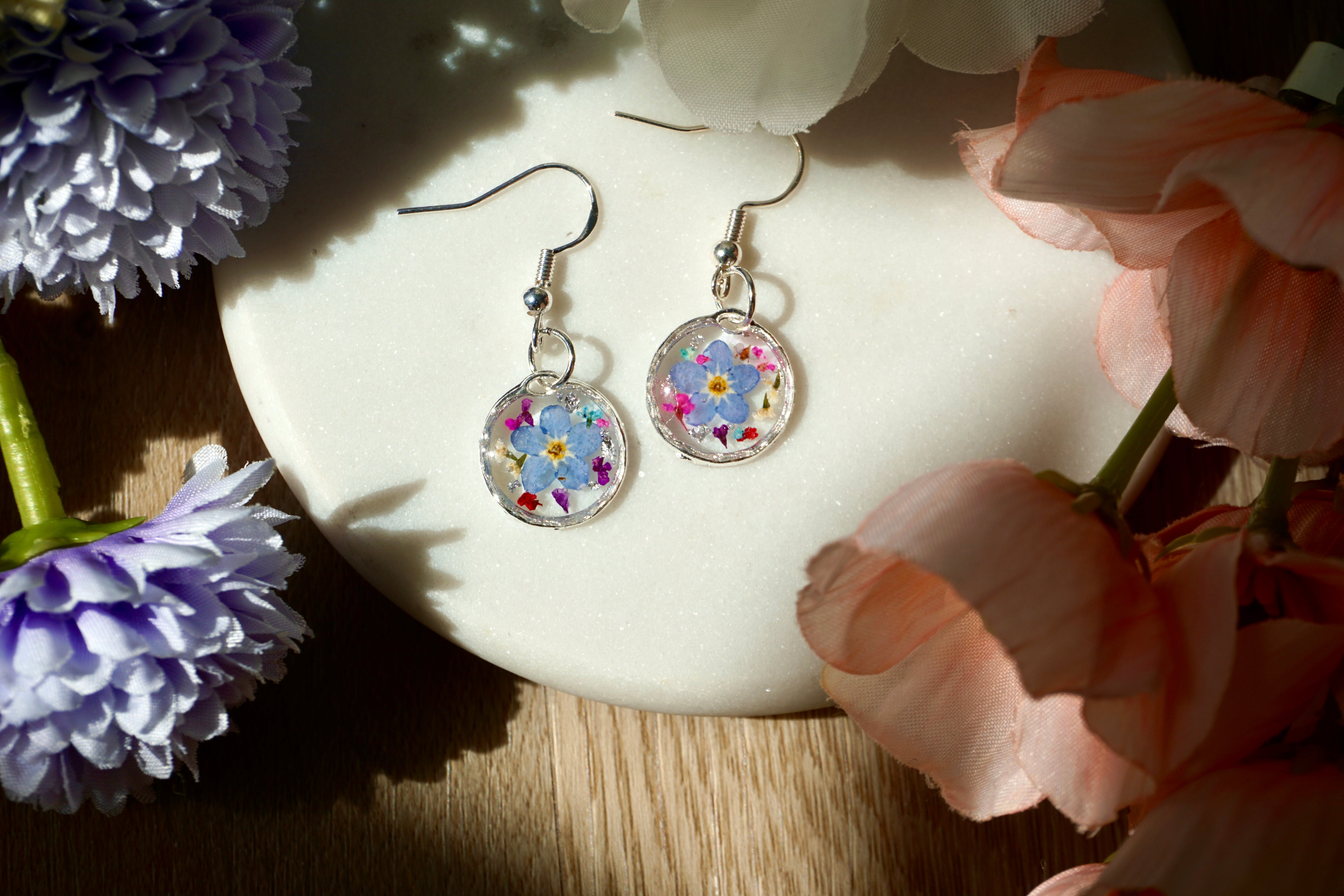 Colorful floral earrings on a white dish with flowers around