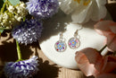 Pair of floral earrings on a white dish with flowers around