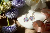 Pair of floral earrings on a white dish with flowers around