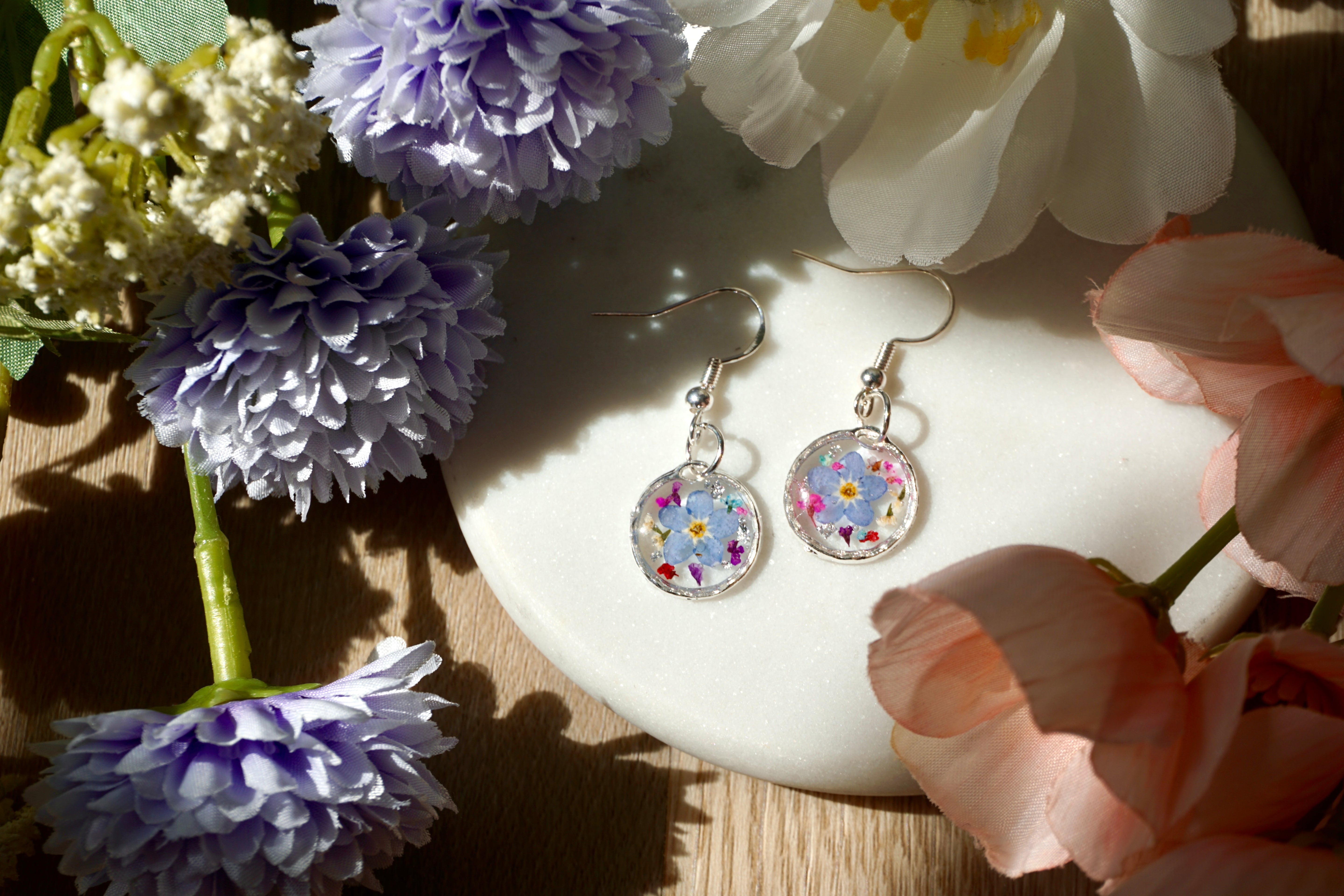 Pair of floral earrings on a white dish with flowers around