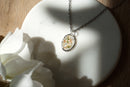 Necklace with a pendant on a white stone surface next to white flowers