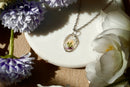 Necklace with a floral pendant on a white dish surrounded by flowers