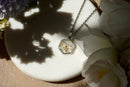 Necklace with a floral pendant on a white dish surrounded by flowers