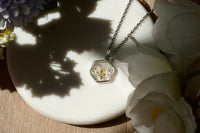 Necklace with a floral pendant on a white dish surrounded by flowers