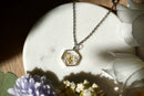 Necklace with a hexagonal pendant on a marble surface with flowers