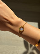 Gold bracelet with a floral design on a wrist against a neutral background