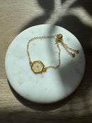 Gold bracelet with a hexagonal pendant on a marble surface