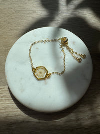 Gold bracelet with a hexagonal pendant on a marble surface