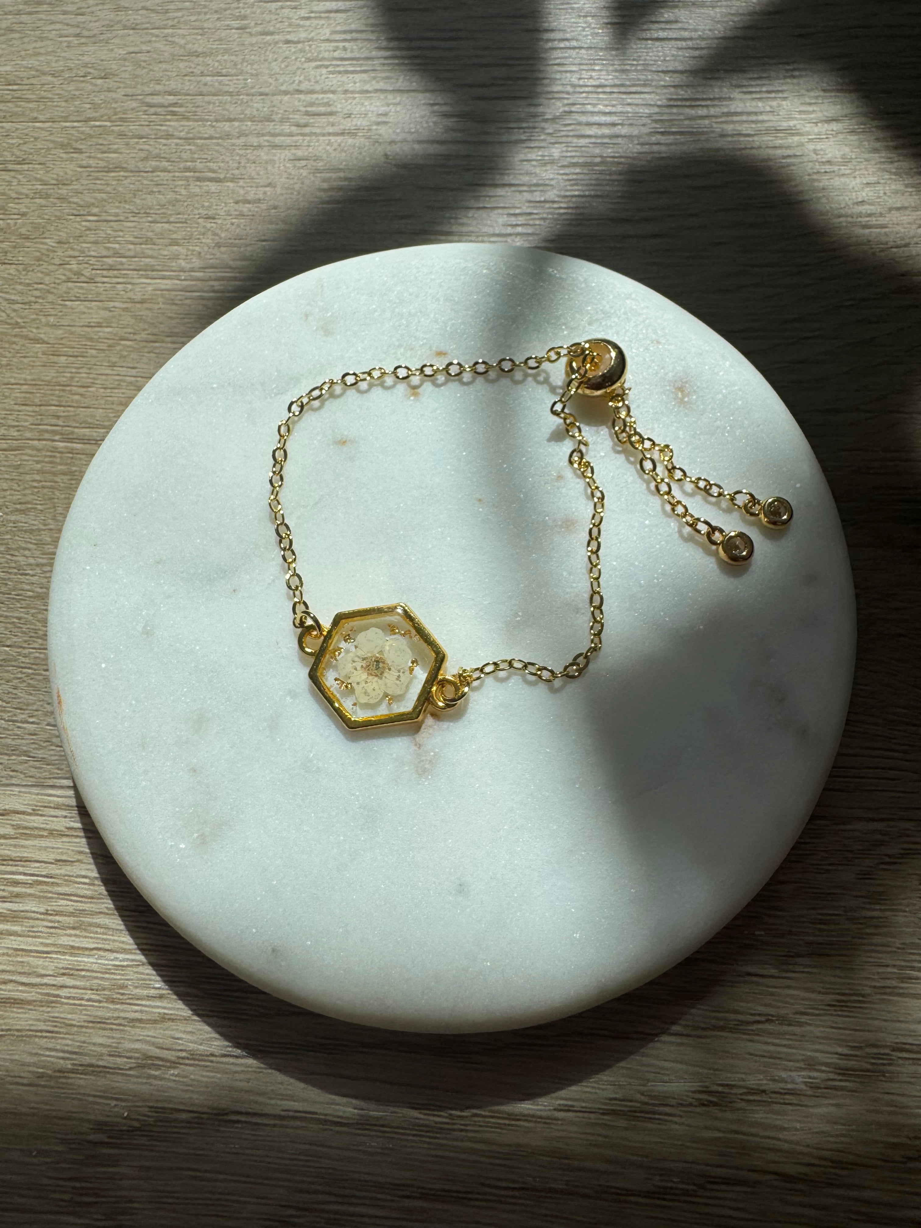 Gold bracelet with a hexagonal pendant on a marble surface