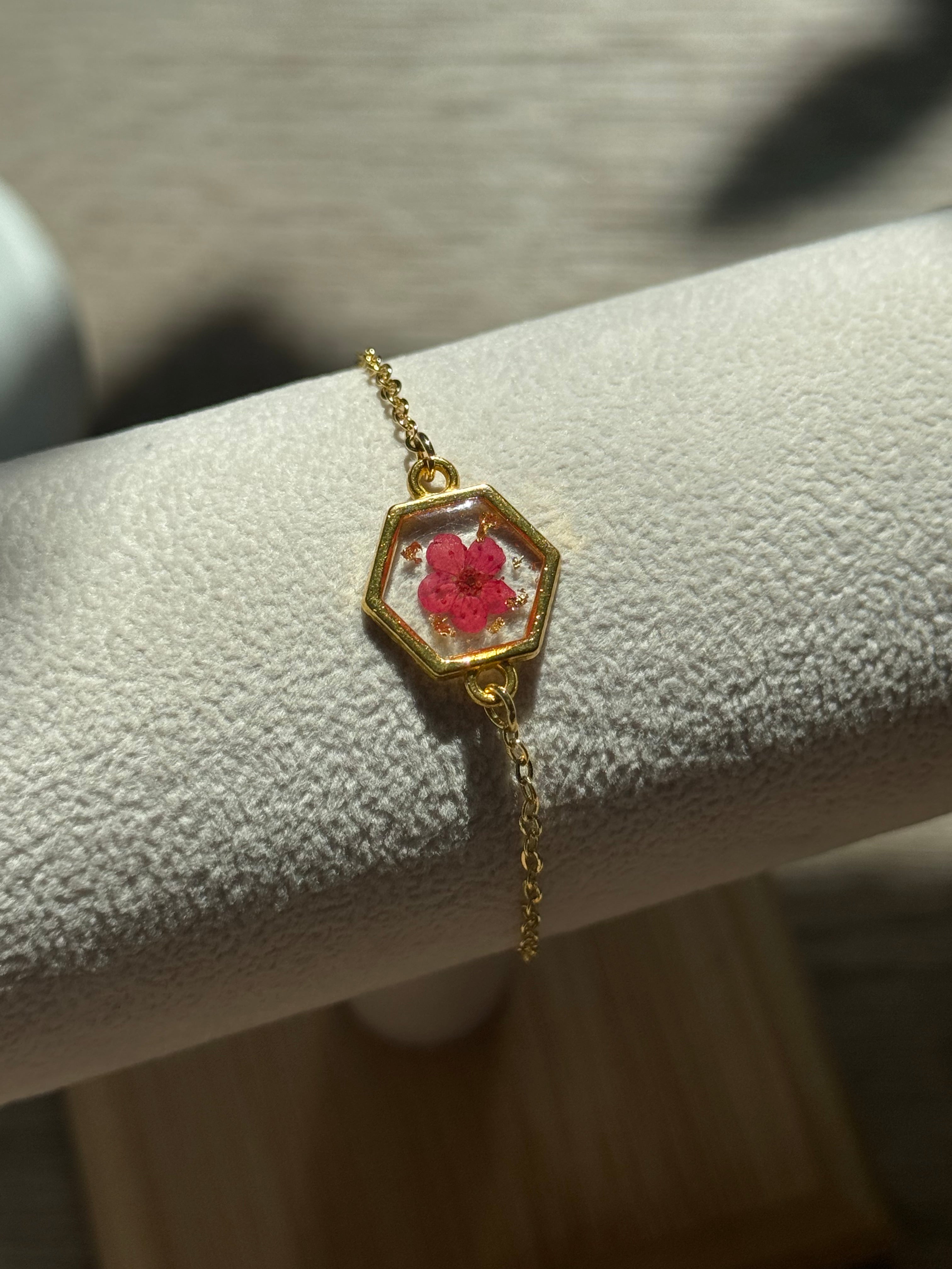 Gold bracelet with a hexagonal charm featuring a red flower on a neutral background